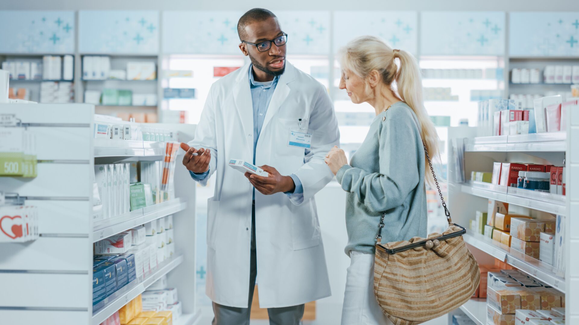 Pharmacy: Professional Black Helpful Pharmacist Advising Caucasian Senior Female Customer with Medicine Recommendation, Talking. Cusotmer Support in Drugstore Full of Drugs, Pill, Health Care Products